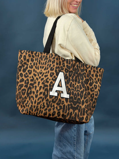 Person holding a leopard print tote bag with a white letter 'A' on a blue background
