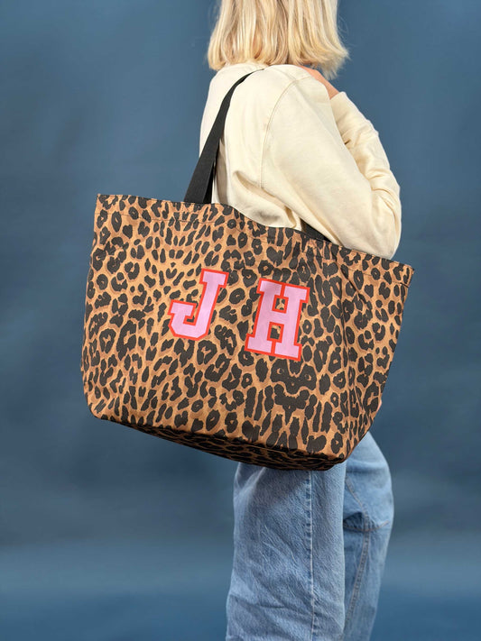 woman holding a large leopard print shopping tote bag printed with the initials 'JH' in pink and red varsity style font