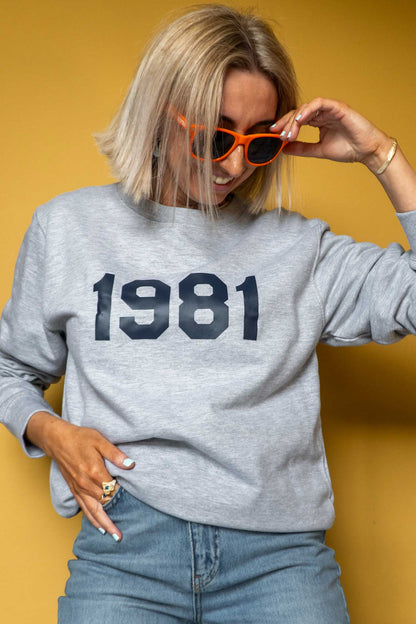 Person wearing a grey sweatshirt with '1981' printed on it in navy