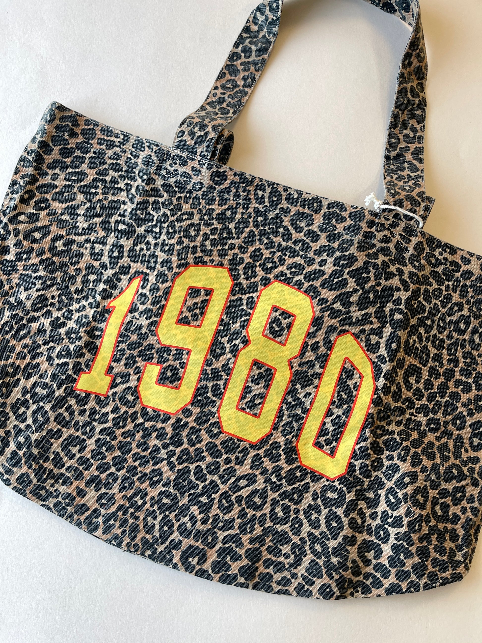 Leopard print tote bag with '1980' print in yellow and orange on a white background