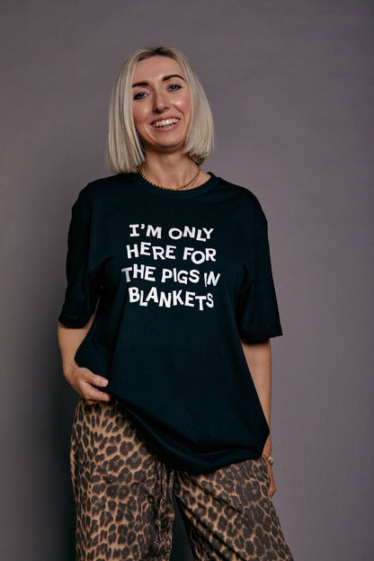 Person wearing a black t-shirt with 'I'm only here for the pigs in blankets' text, standing against a plain background