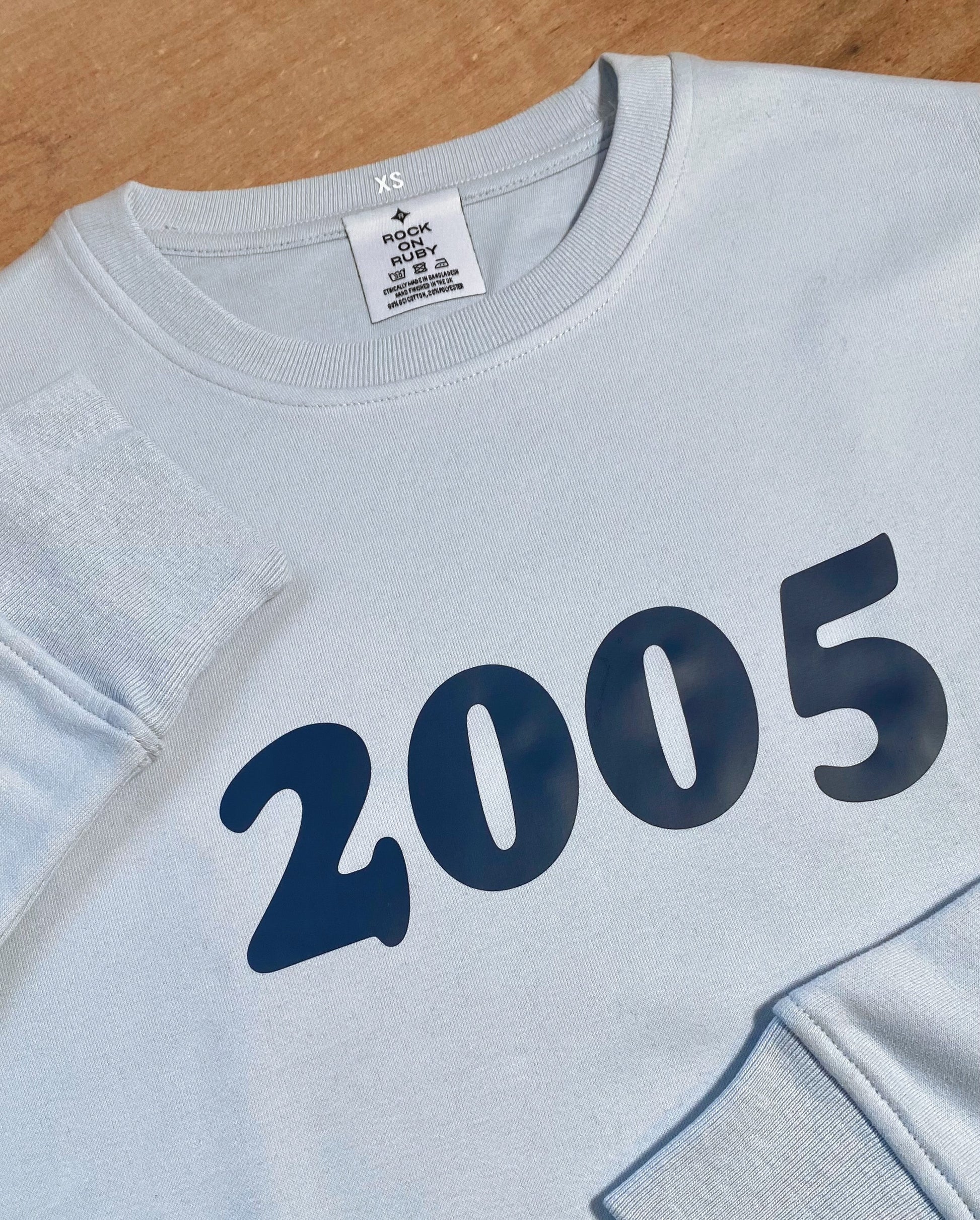 rock on ruby sweatshirt in pale blue printed with '2005' in a navy blue, retro style font on the front
