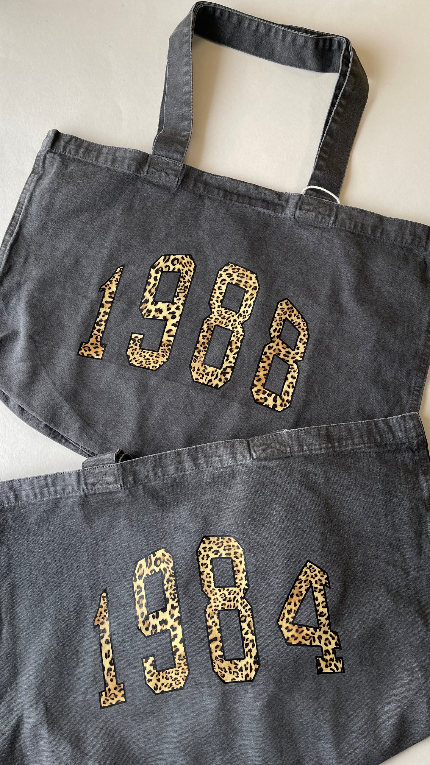 Two dark denim bags with '1984' printed in leopard print on a light background