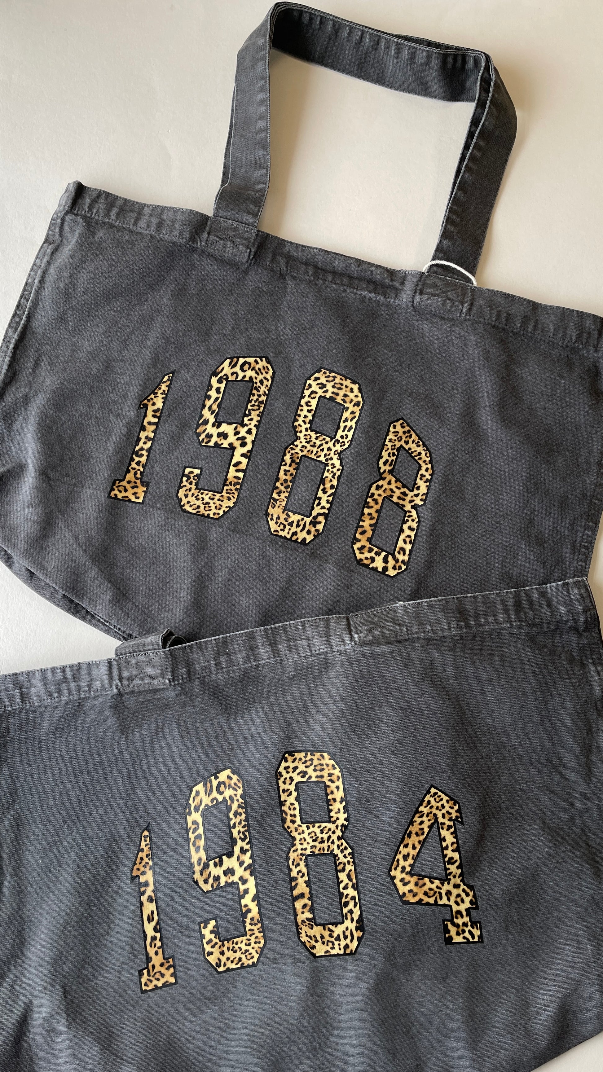 Two dark denim bags with '1984' printed in leopard print on a light background