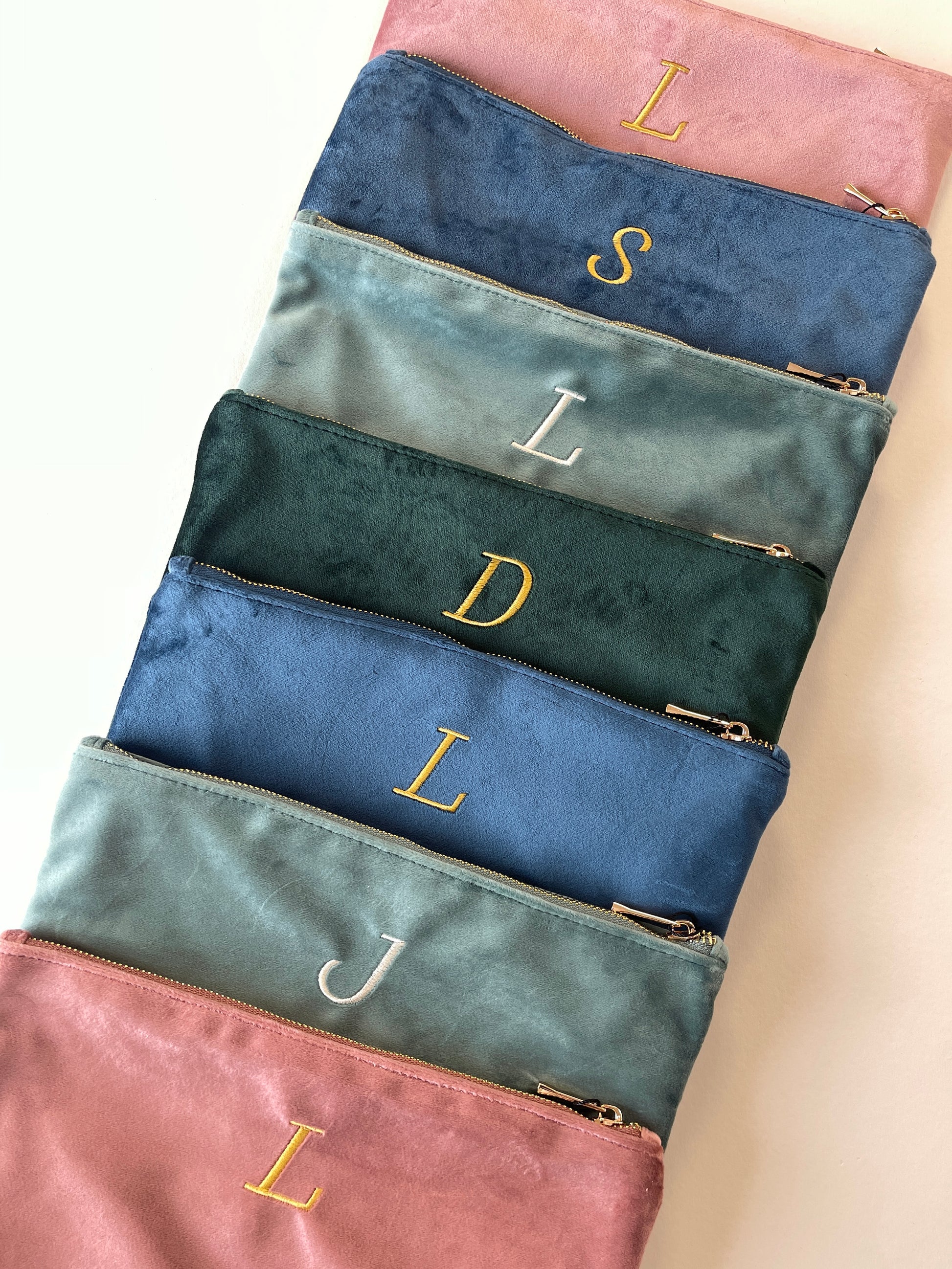 Set of colorful pouches with gold monogram initials on a neutral background