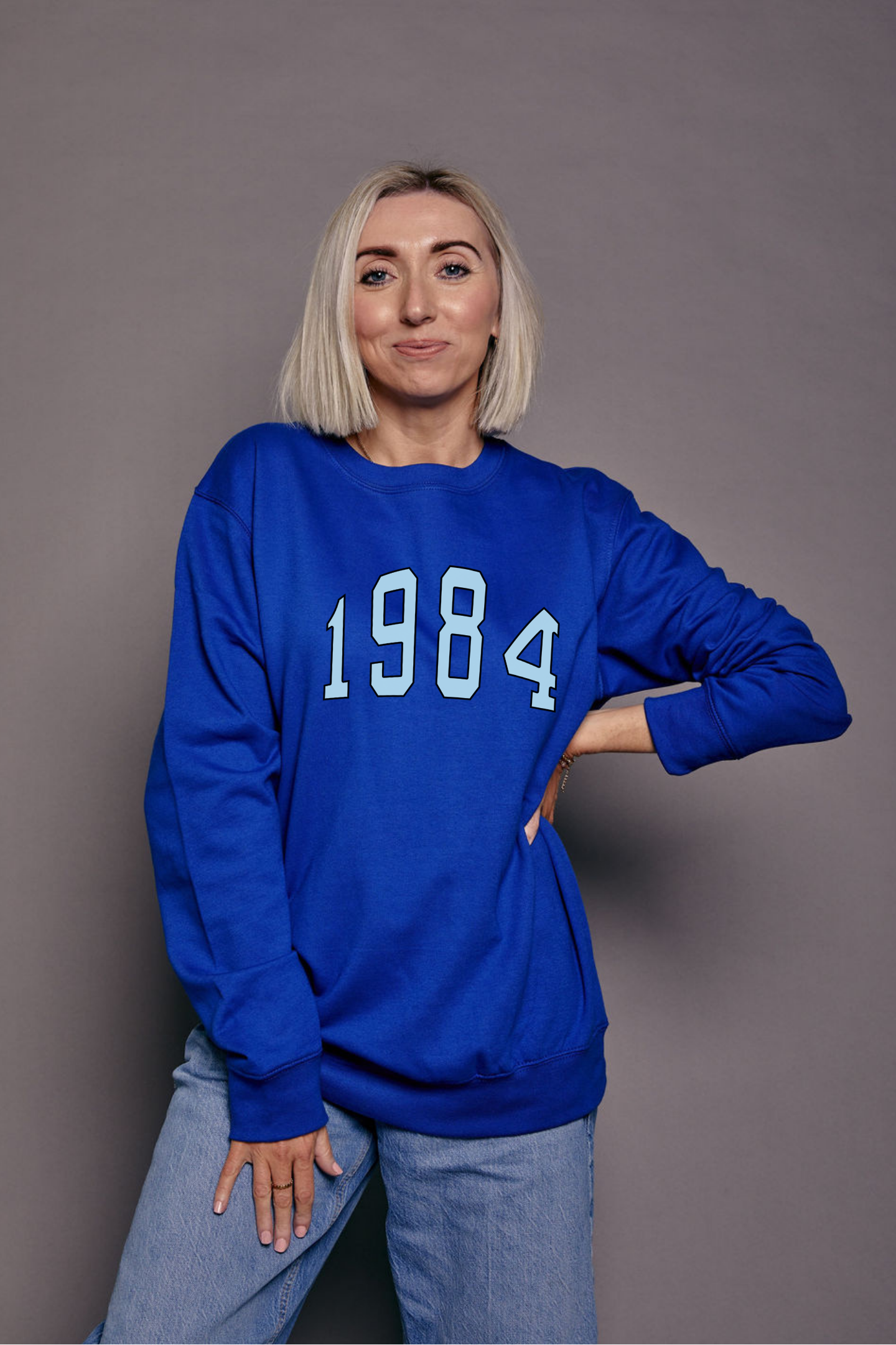 Person wearing a bright blue sweatshirt with '1984' printed on it in pale blue against a grey background