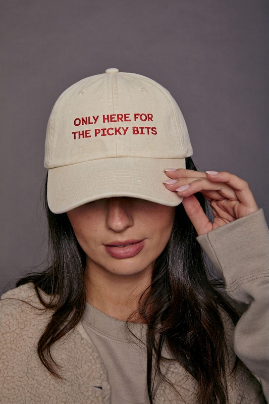 Person wearing a beige cap with red text 'only here for the picky bits' against a grey background