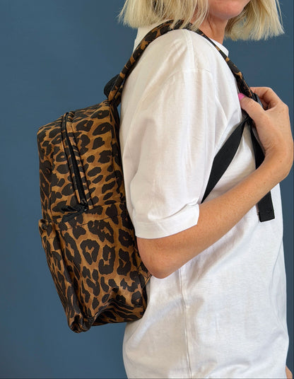 A person wearing a white t-shirt and carrying a leopard print backpack against a solid dark blue background.