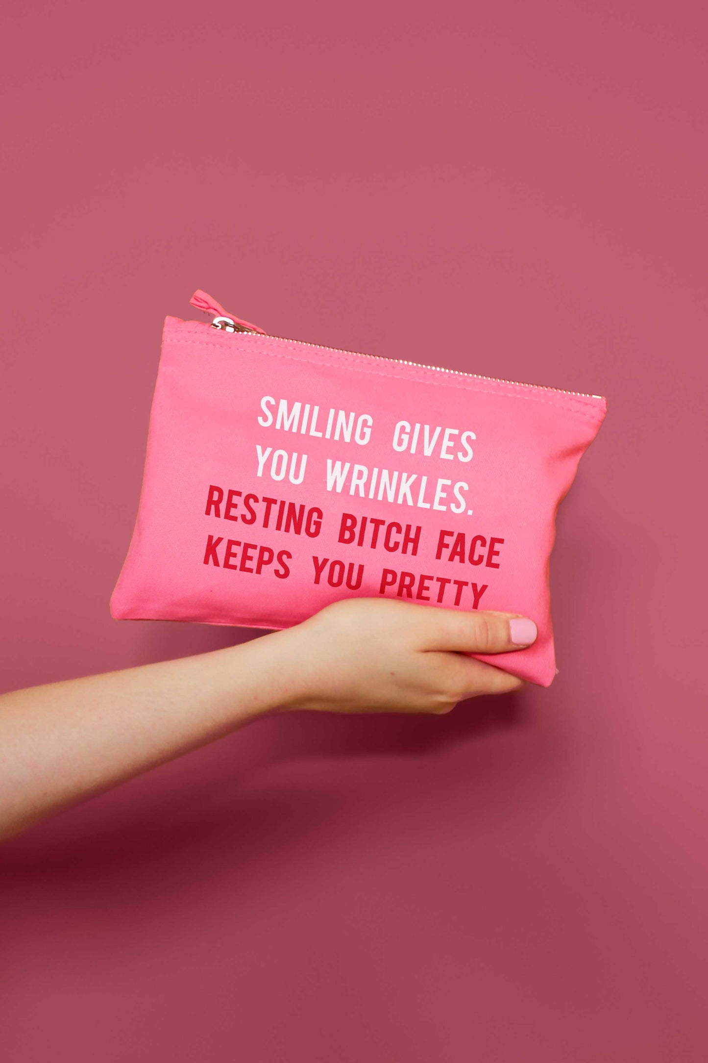 Pink pouch with humorous text held by a hand against a pink background
