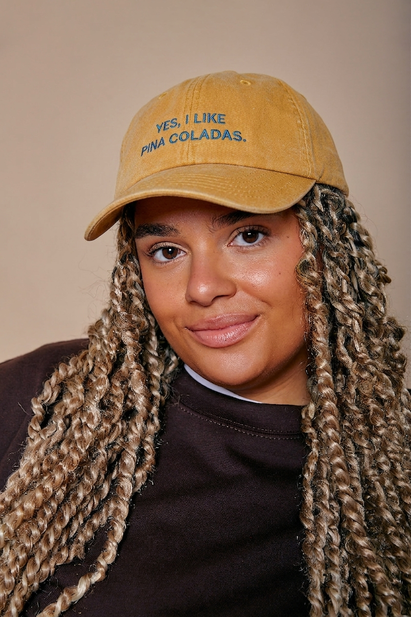 Person wearing a tan cap with 'YES, I LIKE PINA COLADAS.' text against a beige background