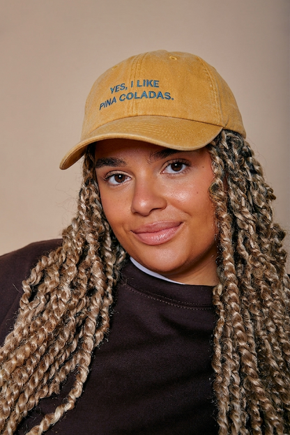 Person wearing a tan cap with 'YES, I LIKE PINA COLADAS.' text against a beige background