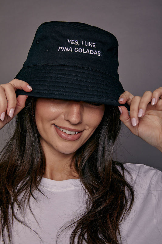Person wearing a black bucket hat with 'YES, I LIKE PINA COLADAS.' text against a gray background